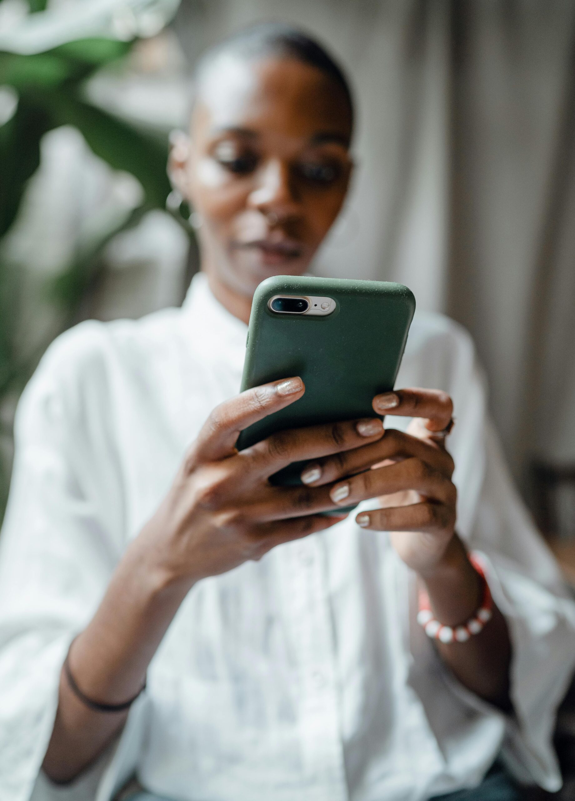 A woman in a white blouse using her smartphone indoors, showing a thoughtful and calm mood.